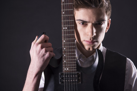 Young guitarist with the electric guitar, isolated on dark background is looking at the camera.の写真素材