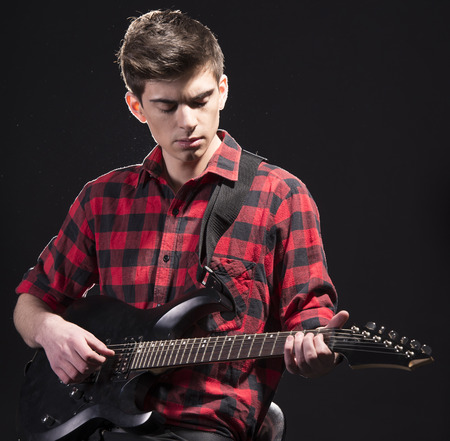 Young male musician is playing a six-string bass guitar on dark background.の写真素材