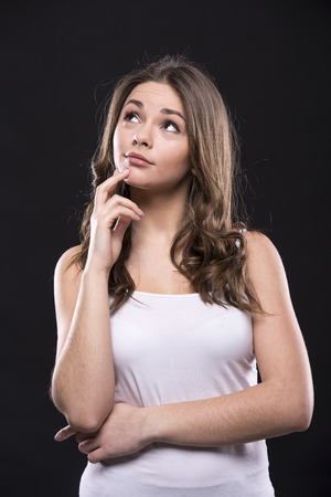 Portrait of a young woman is standing on dark background and looking away and thinking about something.の写真素材