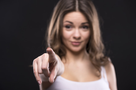 Blurred young woman is pointing at you on dark background.の写真素材
