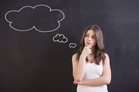 Young woman is standing in front of blackboard, looking away and thinking about something. Young woman is standing in front of blackboard, looking away and thinking about something.