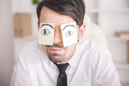 Close-up a tired businessman with adhesive note on his eyes.の写真素材
