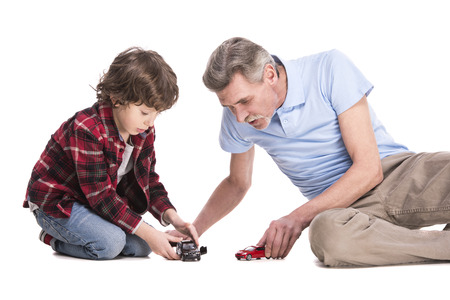Smiling grandfather and his grandson are playing with cars, over the white background.