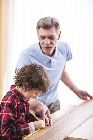 Grandfather and grandson are measuring a table with measuring tape.の写真素材