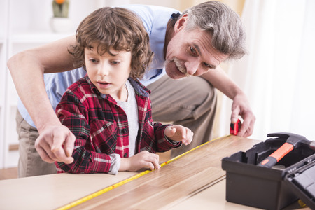 Good time together. Grandfather and grandson are measuring a table with measuring tape.の写真素材