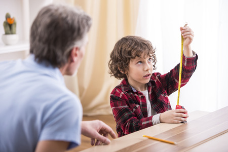 Grandfather and grandson are measuring a table with measuring tape.の写真素材
