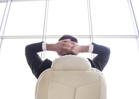 Businessman relaxing in the chair of his office with his hands behind his head.View from the backside.の写真素材