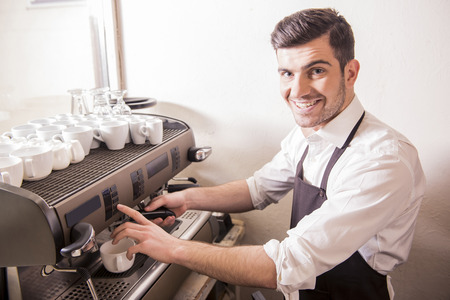 Handsome smiling young barista is making coffee in his cafe.の写真素材