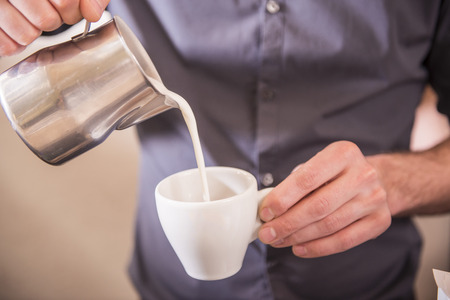 Barista hands is pouring milk making cappuccino.の写真素材