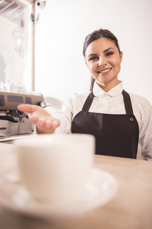 Pretty young barista is offering cup of coffee in a cafe.の写真素材
