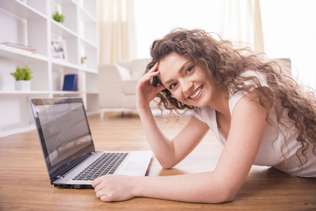 Happy girl is lying on the floor and is working on a laptop. Looking at camera.の写真素材