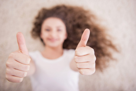 Smiling beautiful woman is lying on the floor and is showing thumb up. Blurred background.の写真素材
