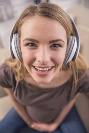 Portrait of pregnant woman is sitting on sofa at home and is listening music in headphones.の写真素材