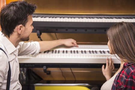Young girl is playing the piano with man in the music store.の写真素材