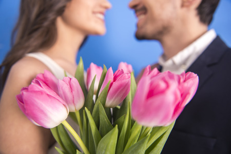 Portrait of young couple in love with flowers tulips are posing at studio. Blurred background.の写真素材