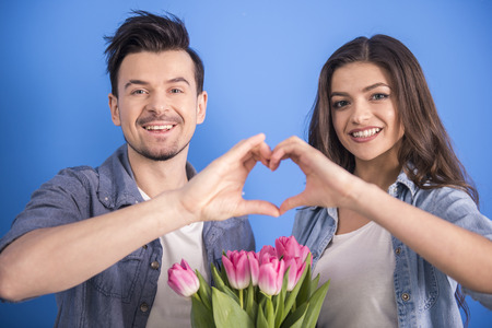 Young couple in love make a heart and hands are holding a bouquet of tulips.