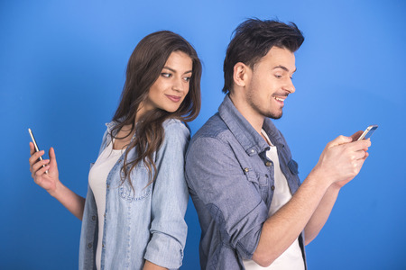 Attractive young couple are looking at smartphone on blue background.の写真素材