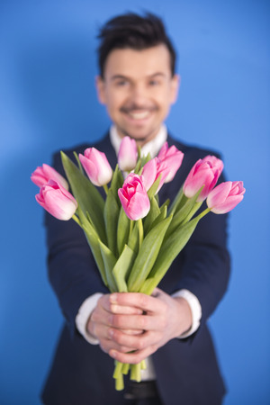 A man is holding out a bunch of tulips isolated on blue background.の写真素材