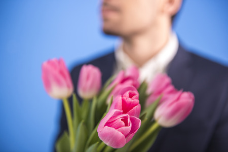 Close-up man is holding a bouquet of tulips isolated on blue background. Blurred background.の写真素材