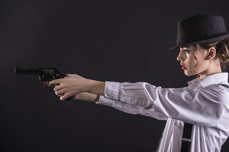 Beautiful and dangerous. Young female gangster holding the gun. isolated on dark background.の写真素材