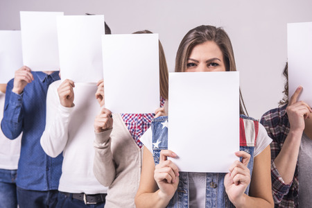 Young group holding a white board and cover their faces. isolated on grey background.の写真素材