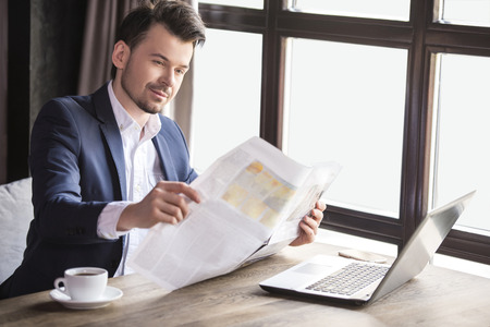 Handsome young businessman reading newspaper with cup of coffee in restaurant.の写真素材