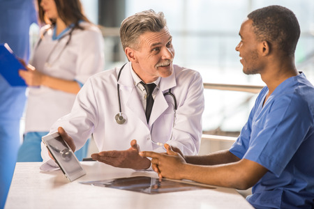 Senior doctor and young doctor talking and using a tablet.の写真素材