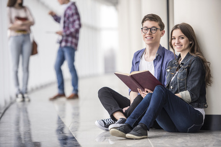 Young couple students sitting and reading a book in corridor in college. And looking at camera.の写真素材