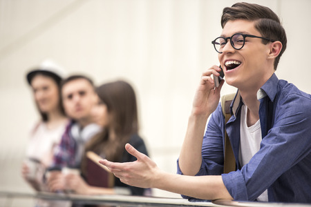 Handsome young student talking on the phone. His classmates in the background.の写真素材