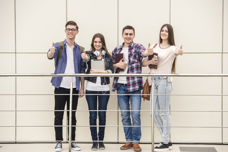 Group of happy young students showing thumbs up in a college. Looking at camera.