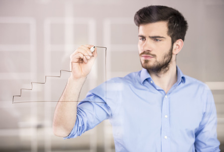 Young handsome businessman drawing on glass screen in office.の写真素材