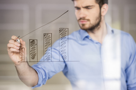Young handsome businessman drawing a graph on glass screen in office.の写真素材