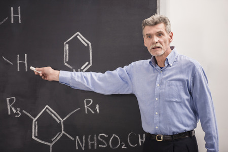 Professor of chemistry writes on the blackboard formula in University.の写真素材