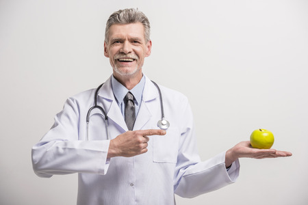 Senior male doctor holding green apple on grey background.の写真素材