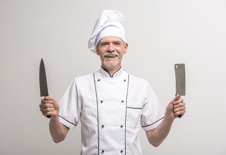 Senior male chief cook in uniform holding knifes a  on grey background.の写真素材