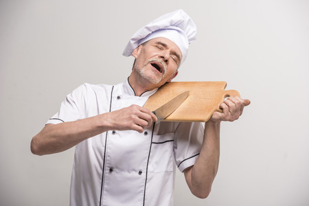 Senior male chief cook in uniform holding knife and  chopping board a  on grey background.の写真素材