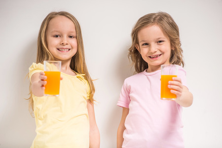 Best friends. Two cute little girls holding juices on grey background.の写真素材