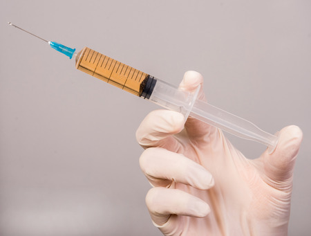 Hand in glove with syringe on grey background.