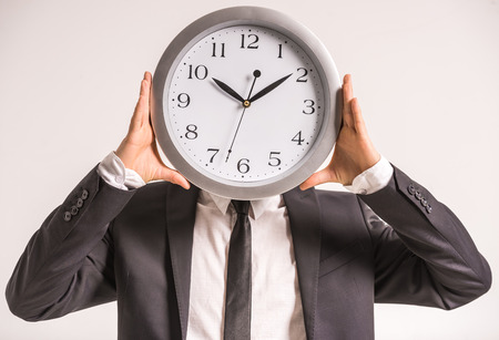 Businessman is holding a clock in front of head.の写真素材