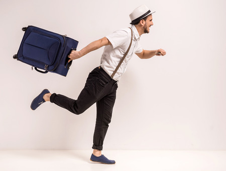 Young creative man is posing with suitcase on grey background.の写真素材