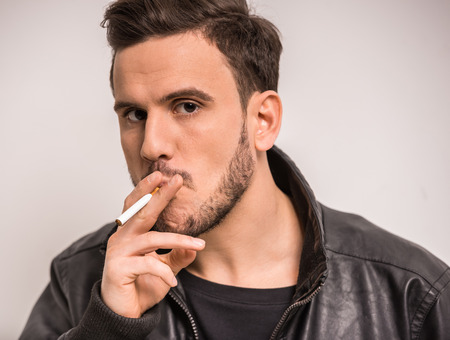 Young stylish man is smoking a cigarette. Gray background.の写真素材
