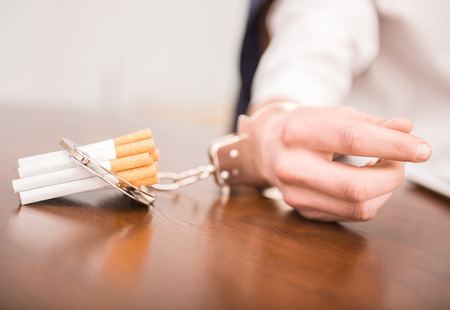 Man hand with handcuffs and cigarettes on the table. The concept of smoking dependence.の写真素材