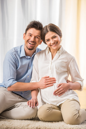 Happy young couple expecting a baby. They are sitting on the carpet on the floor.の写真素材