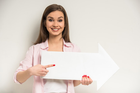Young smiling beautiful girl standing on grey background and holding empty paper billboard with copy space for text.の写真素材
