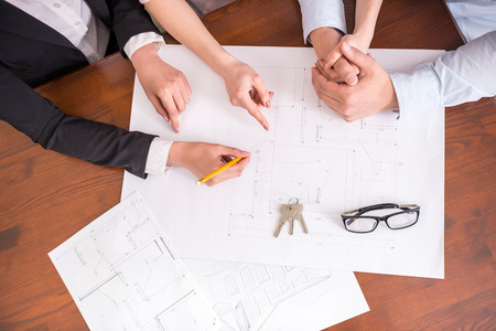 Female realtor showing contract with floor layout in an apartment to a young couple. Close-up.