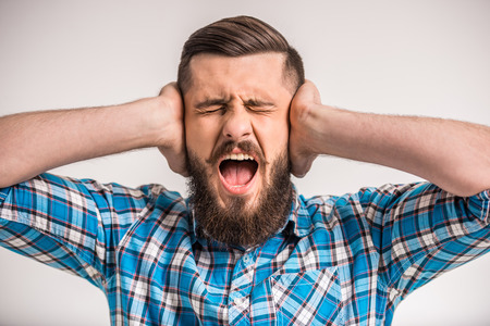Bearded young man closes his ears and shouting.の写真素材