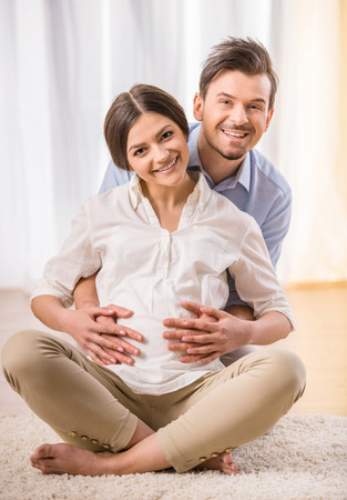 Happy young couple expecting a baby. They are sitting on the carpet on the floor.の写真素材