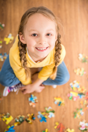 Little pretty smiling girl in yellow  pullover sitting on the floor and playing with puzzle.の写真素材