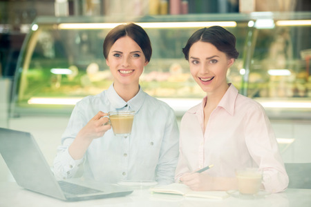 Two young beautiful businesswomen  sitting in urban cafe and using laptop.の写真素材