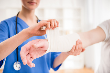 Close-up of female doctor with stethoscope  bandaging hand of male patient.の写真素材